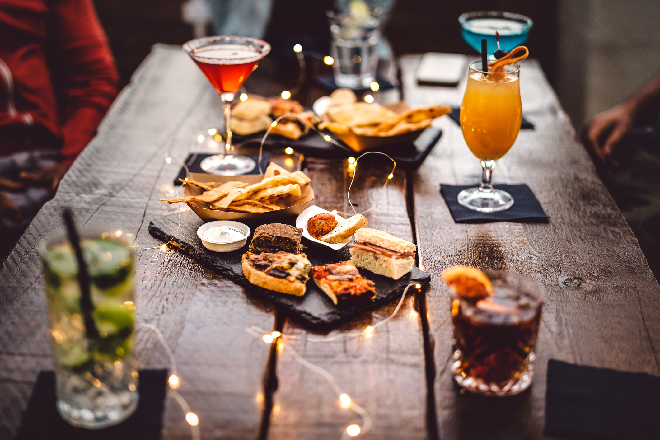 Blurred background of multicolored drinks and minimal food – Happy hour concept with fancy cocktails and tasty appetizers served at rooftop lounge prive – Warm vintage filter on shallow depth of field